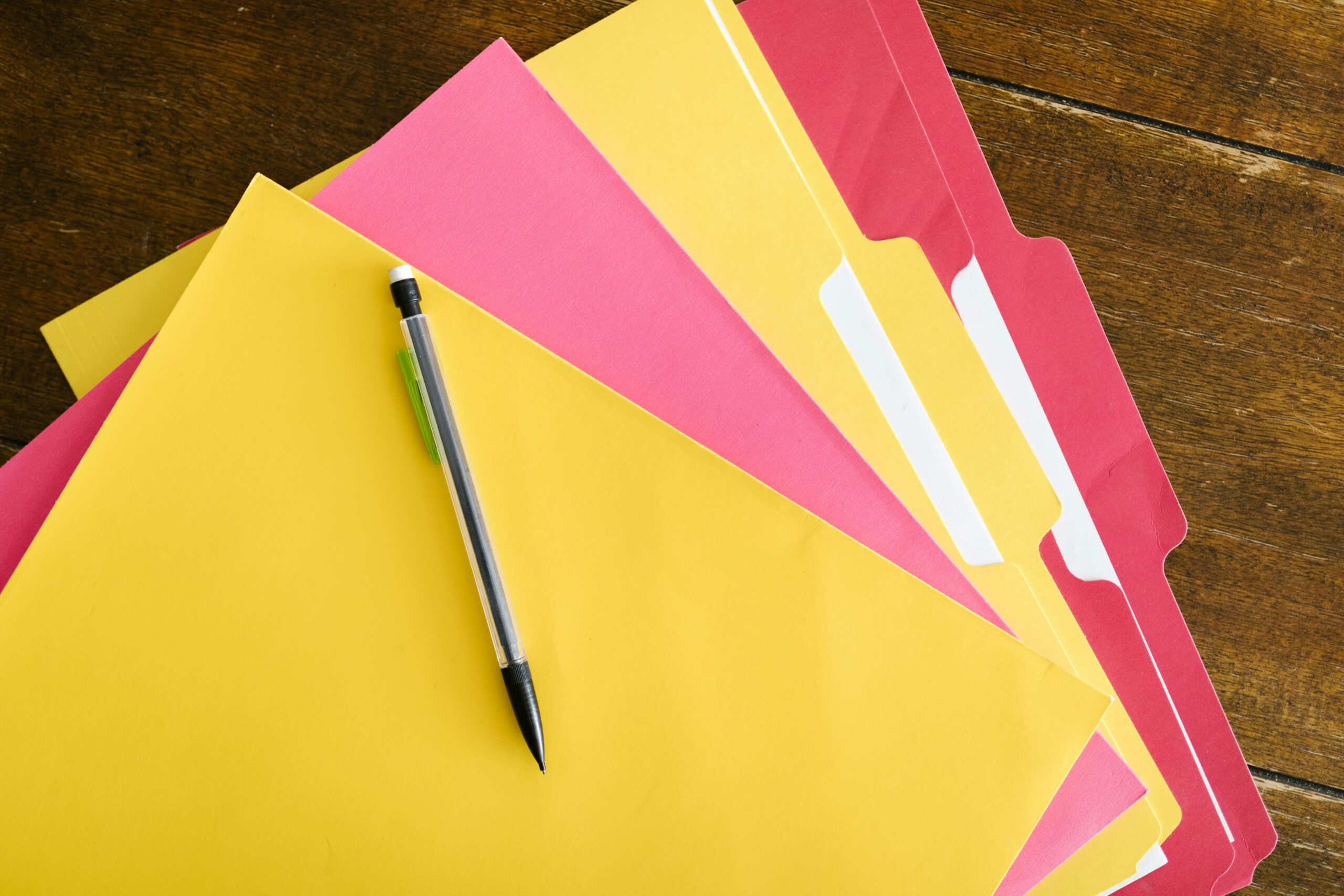 Colorful folders and pen arranged on a wooden table for office organization.